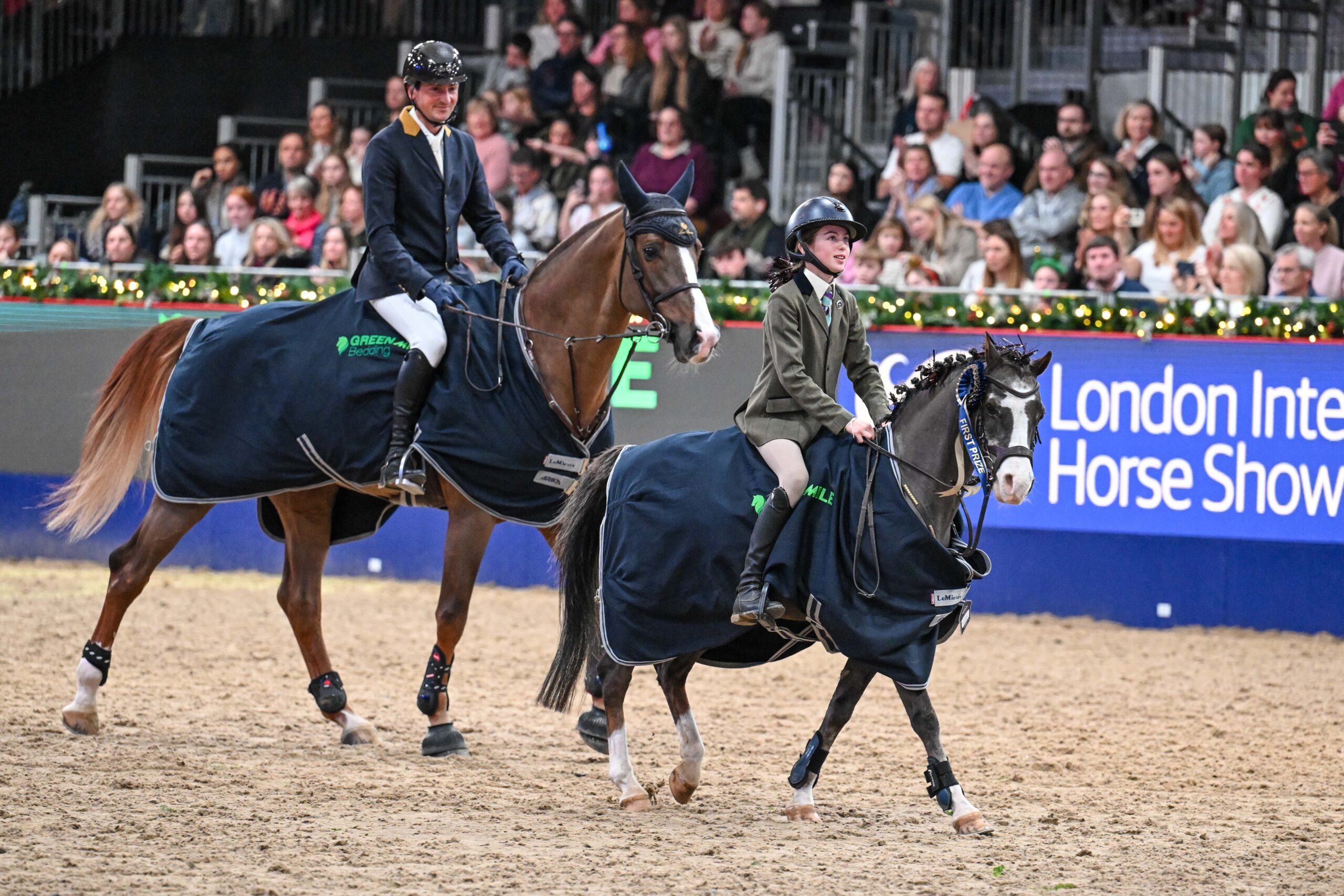 a man and woman riding horses in a arena with a crowd watching